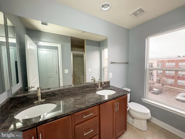 a bathroom with a granite countertop sink toilet a large mirror and a window