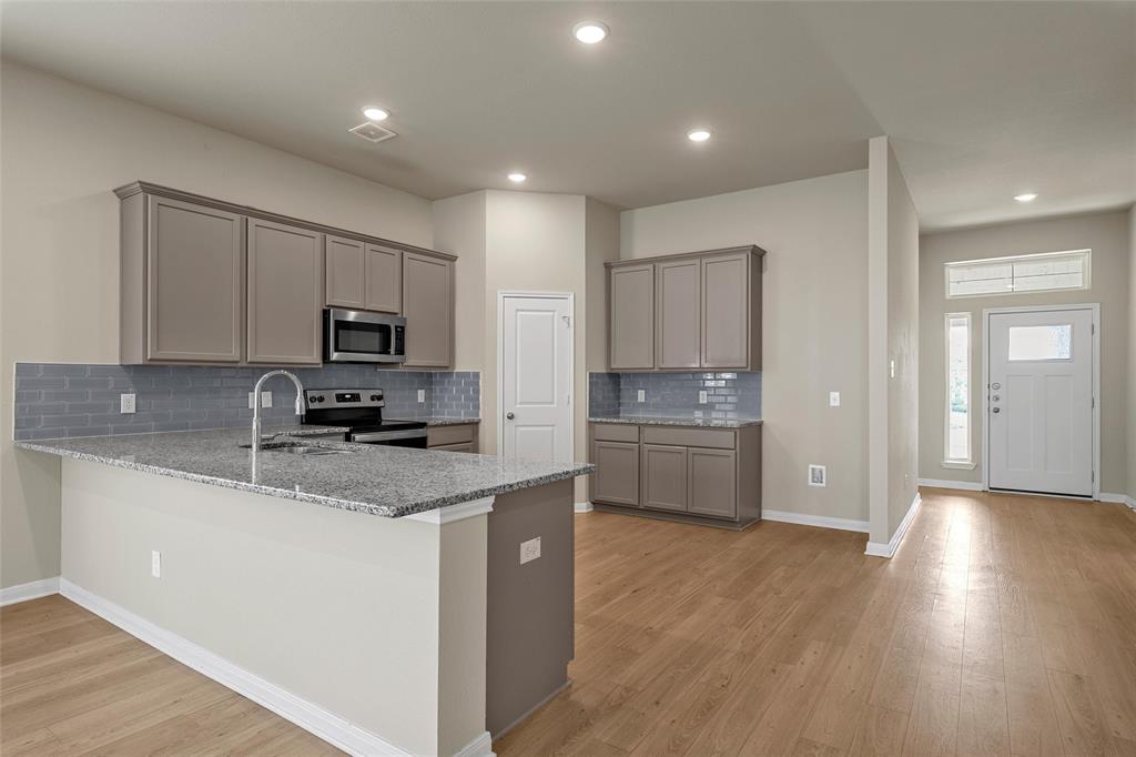 3205 Dottavio Road Lorena, TX 76655 - Photo 9 of 33 Kitchen featuring a granite countertop island with an undermount sink, stainless steel appliances, grey subway tile backsplash, and coordinating cabinetry