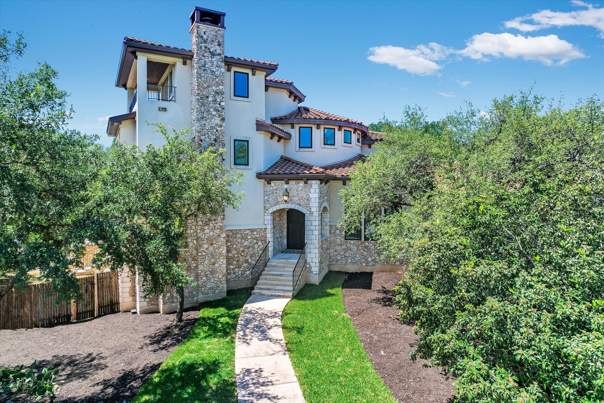 A grand, multi-level home showcases stone and stucco construction, with a prominent stone chimney and a welcoming arched entryway.