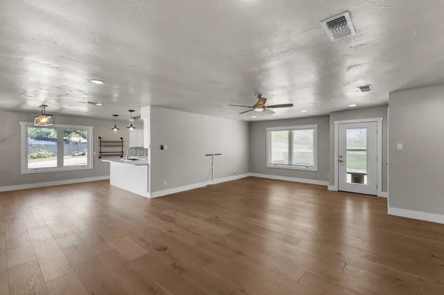 an empty room with wooden floor chandelier and windows