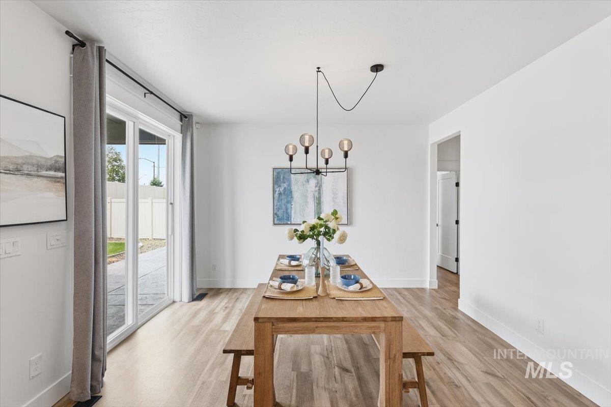 5897 West Riva Capri Street Meridian, ID 83646 - Photo 14 of 50 Bright dining area featuring wood-finish flooring, a modern linear pendant light fixture, and a sliding glass door providing direct access to the exterior