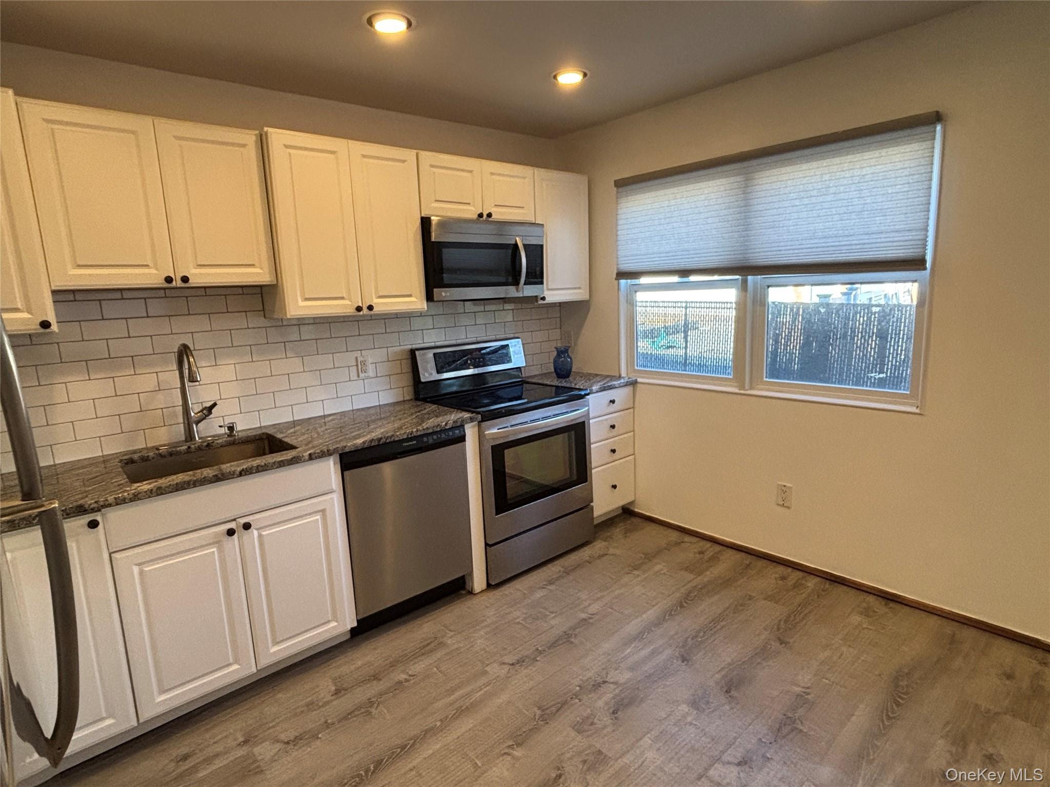40 Canoe Place Road, Unit 4 Hampton Bays, NY 11946 - Photo 12 of 36 a kitchen with granite countertop white cabinets stainless steel appliances a sink and a window
