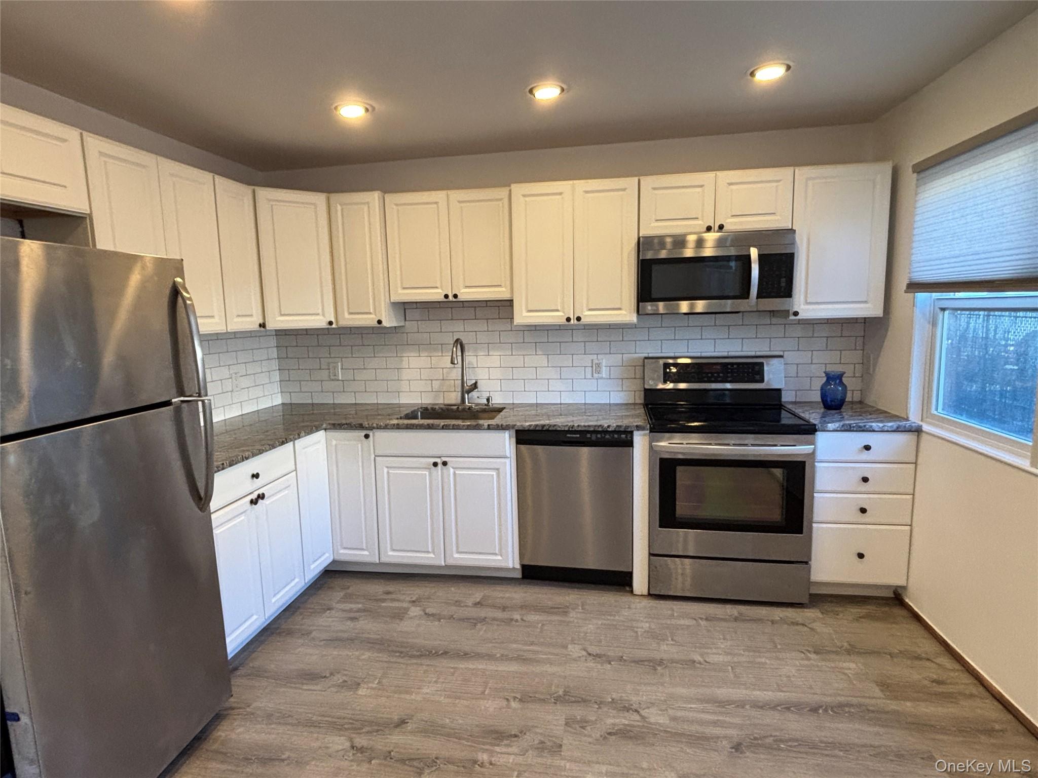 40 Canoe Place Road, Unit 4 Hampton Bays, NY 11946 - Photo 9 of 36 a kitchen with white cabinets stainless steel appliances and a refrigerator