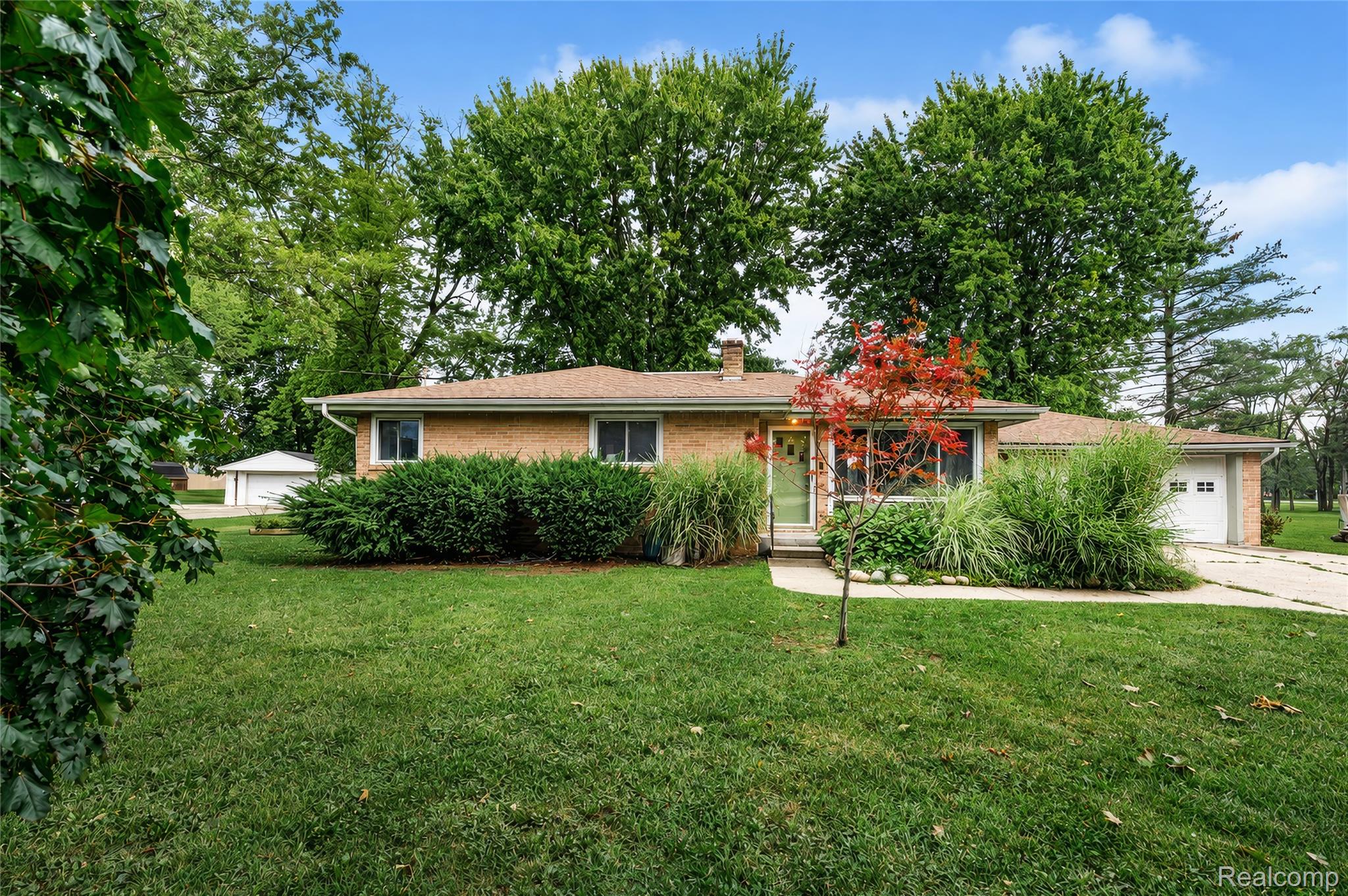 Brick exterior residence featuring a front lawn, mature trees, and an attached garage with a white door