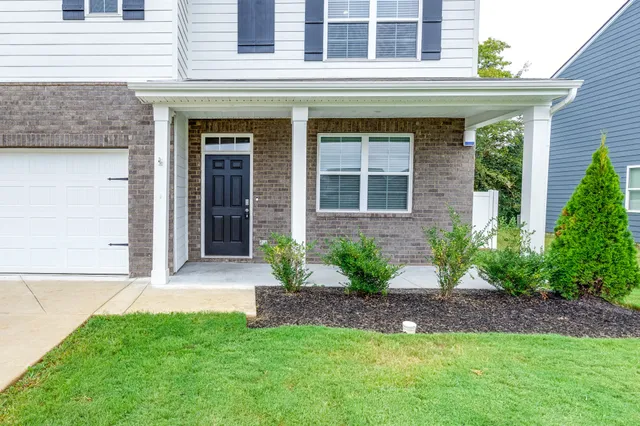 a view of a brick house with a yard plants and large tree