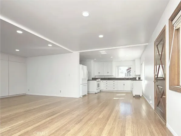 a large white kitchen with a refrigerator a stove and a wooden floors