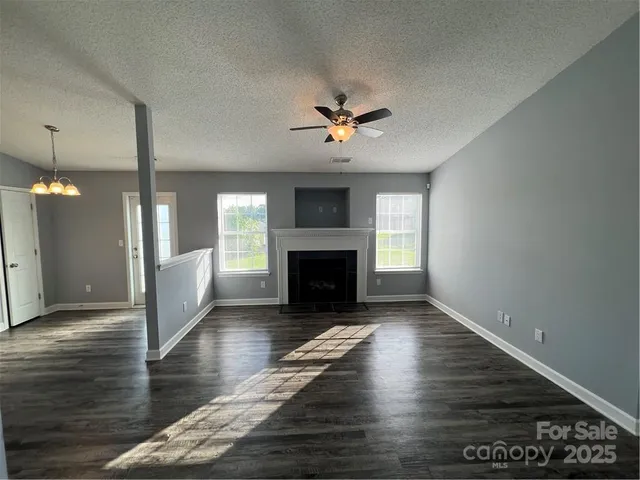 a view of an empty room with wooden floor fireplace and a window