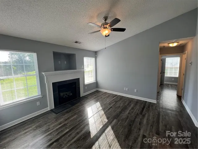 a view of an empty room with wooden floor fireplace and a window