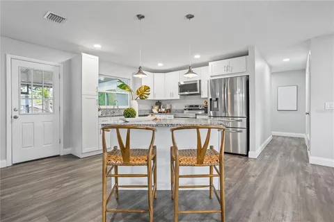 a kitchen with stainless steel appliances kitchen island granite countertop a refrigerator a stove a microwave oven a sink with island and chairs with wooden floor