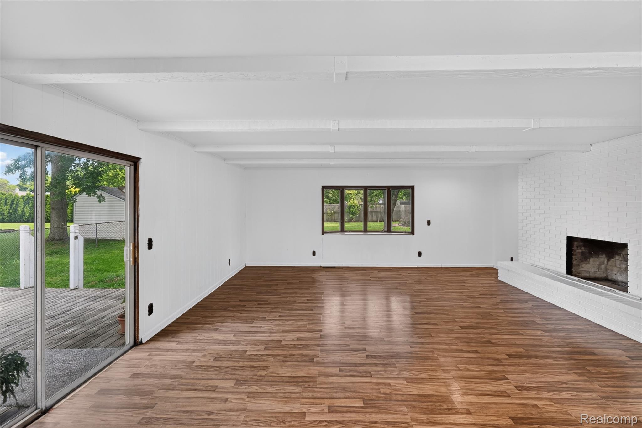 5457 Reid Road Swartz Creek, MI 48473 - Photo 22 of 51 Spacious room featuring wood-finish flooring, a white brick fireplace with a hearth, and exposed white ceiling beams