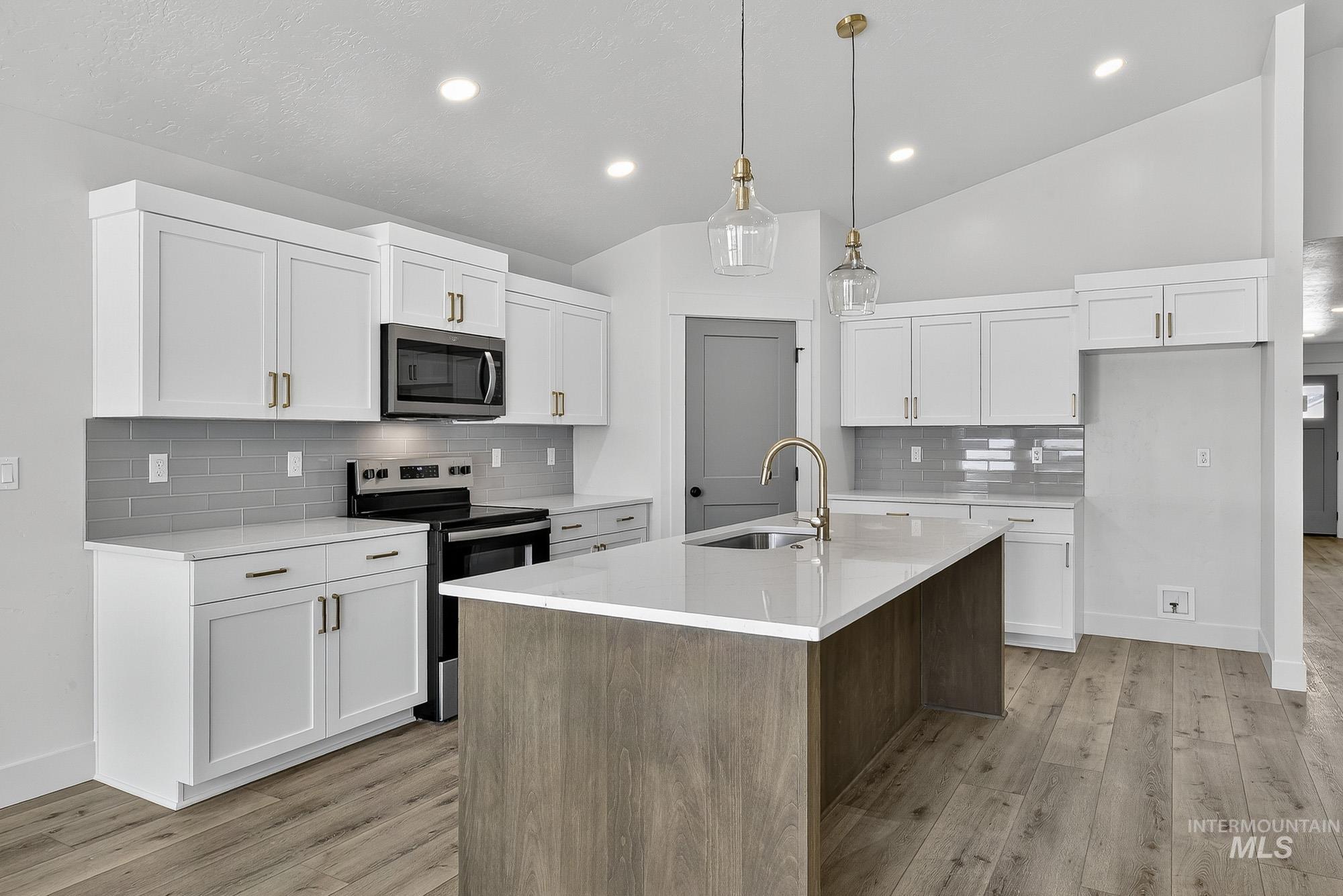 1158 Velvet Loop Wilder, ID 83676 - Photo 9 of 34 Kitchen featuring appliances with stainless steel finishes, white cabinetry, decorative light fixtures, vaulted ceiling, and a center island with sink