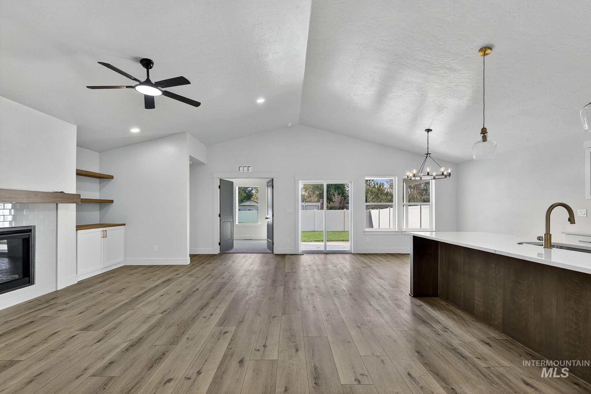1158 Velvet Loop Wilder, ID 83676 - Photo 3 of 34 Unfurnished living room with a glass covered fireplace, light wood-style floors, lofted ceiling, a chandelier, and a textured ceiling