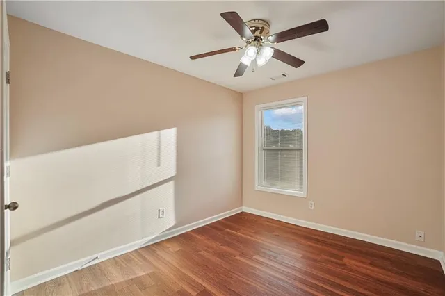 an empty room with wooden floor chandelier fan and windows