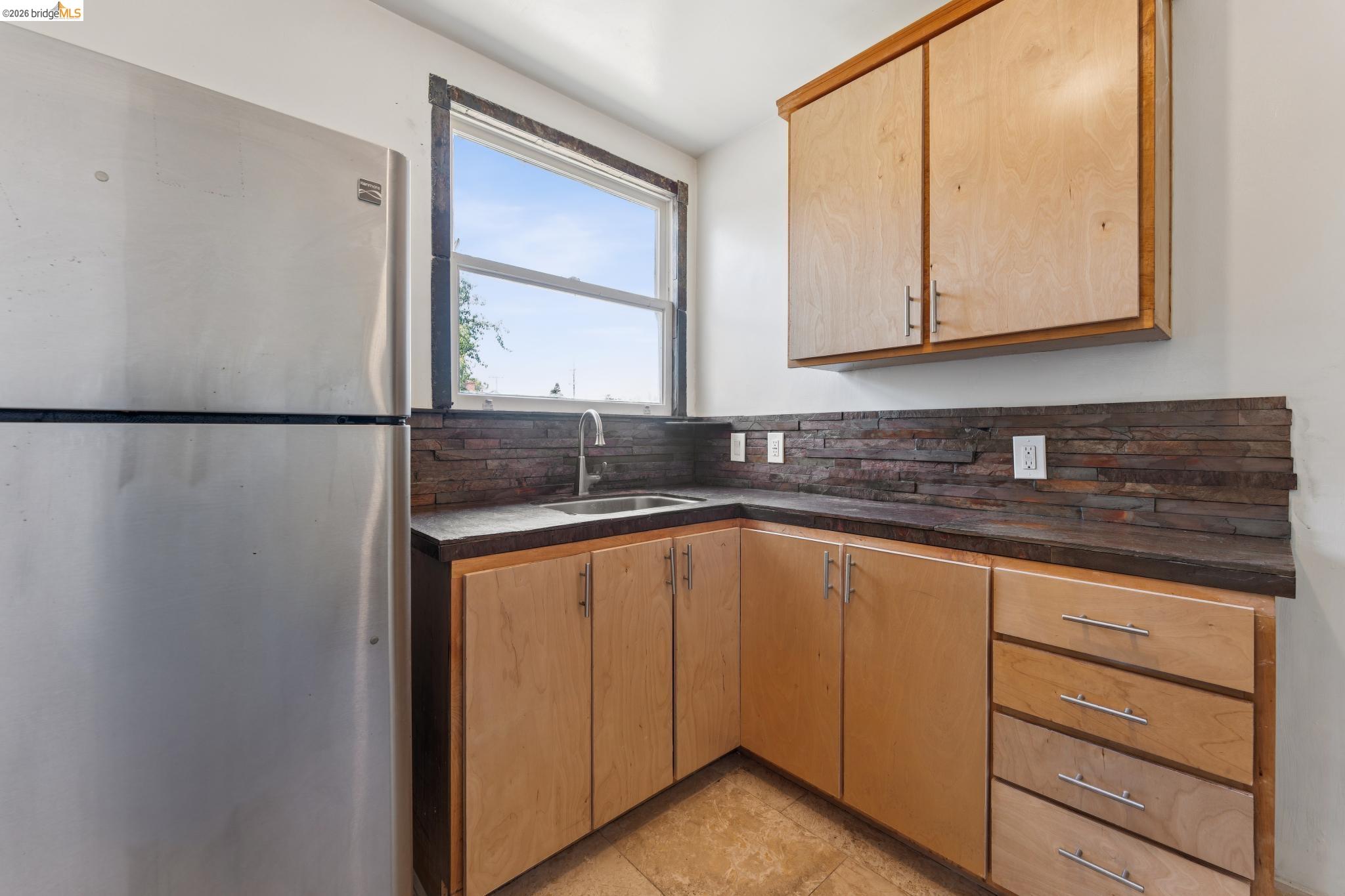 2879 Rheem Avenue Richmond, CA 94804 - Photo 19 of 45 Corner kitchen area featuring light wood cabinetry with brushed nickel hardware, dark countertops, and a stacked stone backsplash