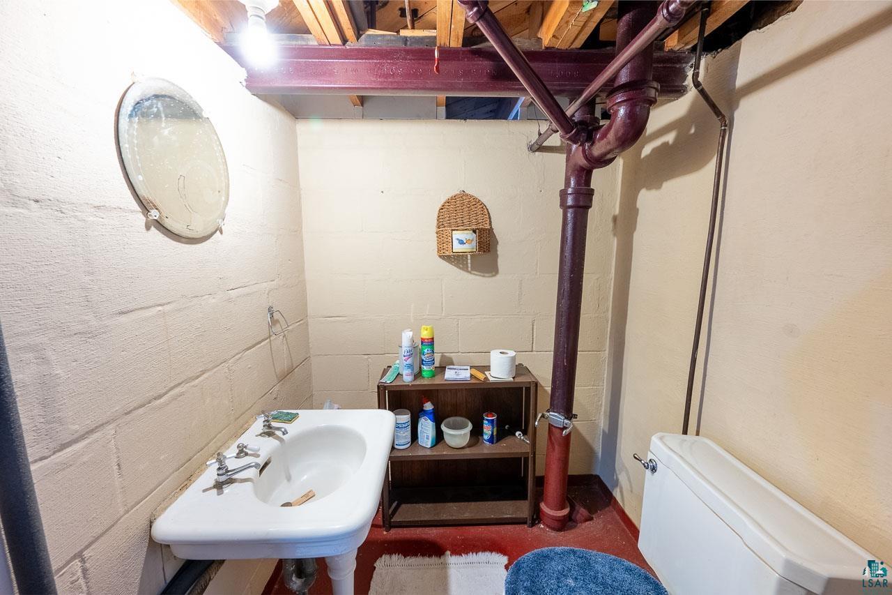 101 2nd Avenue North Biwabik, MN 55708 - Photo 30 of 44 Basement bathroom featuring a wall-mounted sink, exposed overhead joists, visible plumbing, and a commode