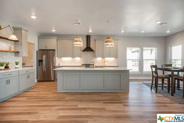 a kitchen with stainless steel appliances granite countertop a refrigerator a sink dishwasher a stove and white countertops with wooden floor