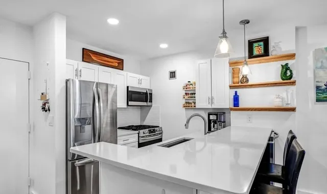 a kitchen with stainless steel appliances a refrigerator a stove a sink a oven with white cabinets and wooden floor