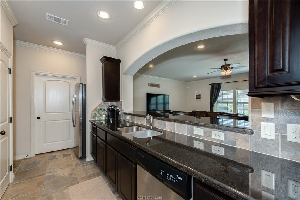 1408 Cres Ridge Drive College Station, TX 77845 - Photo 6 of 19 Kitchen with dark wood finish cabinets, backsplash, stainless steel appliances, light stone finish floors, and ceiling fan