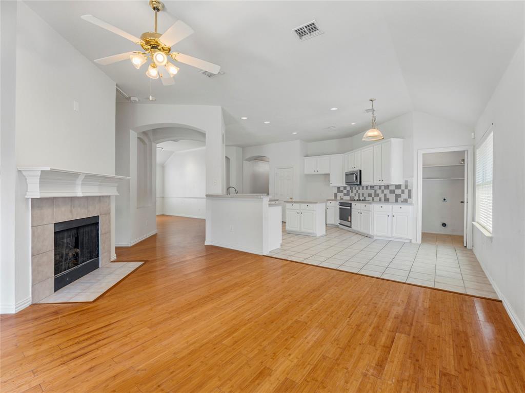 Unfurnished living room with arched walkways, lofted ceiling, ceiling fan, light wood finished floors, and a tile fireplace