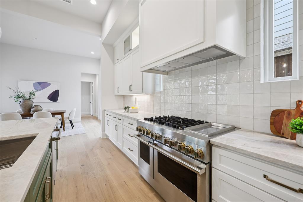 3845 Van Ness Lane Dallas, TX 75220 - Photo 14 of 33 Two tone kitchen with light stone counters, range with two ovens, glass fronted cabinets, light wood finished floors, and backsplash