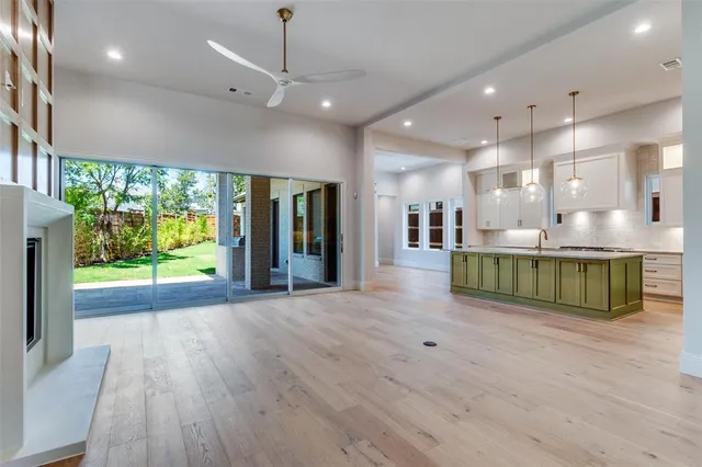 a view of an empty room with kitchen view and wooden floor