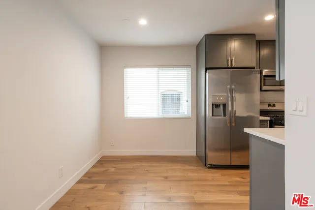an empty room with wooden floor kitchen view and windows