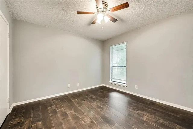 an empty room with wooden floor fan and windows