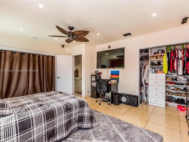 a bedroom with a bed a computer on a table and a flat screen tv