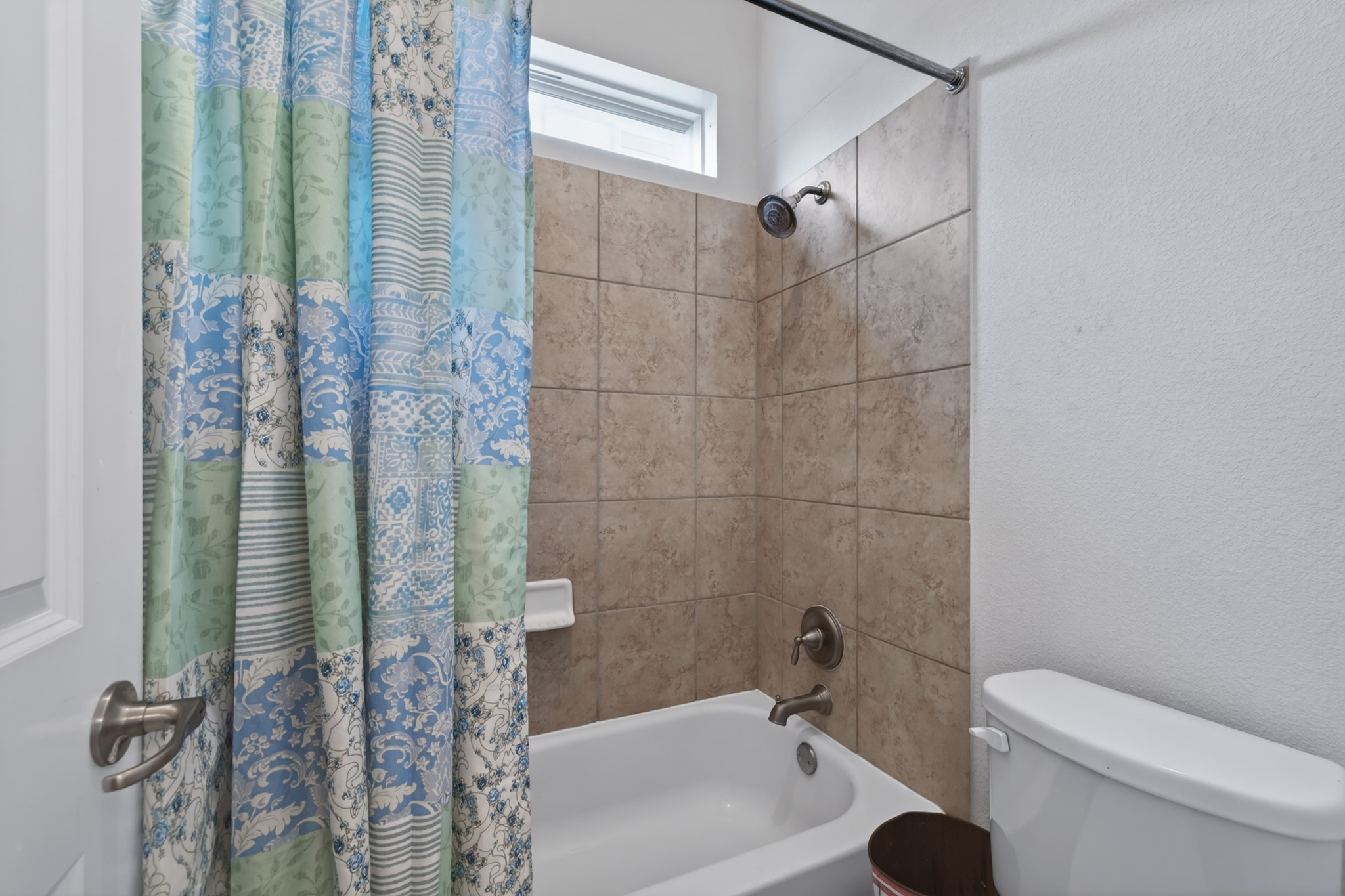 1017 Tabernash Leander, TX 78641 - Photo 29 of 38 Bathroom featuring a white tub-shower combination with bronze fixtures, neutral-toned tile surround, and a high-set window