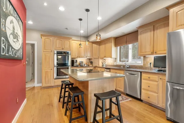 a kitchen with stainless steel appliances kitchen island granite countertop a refrigerator a stove a sink a dining table and chairs with wooden floor
