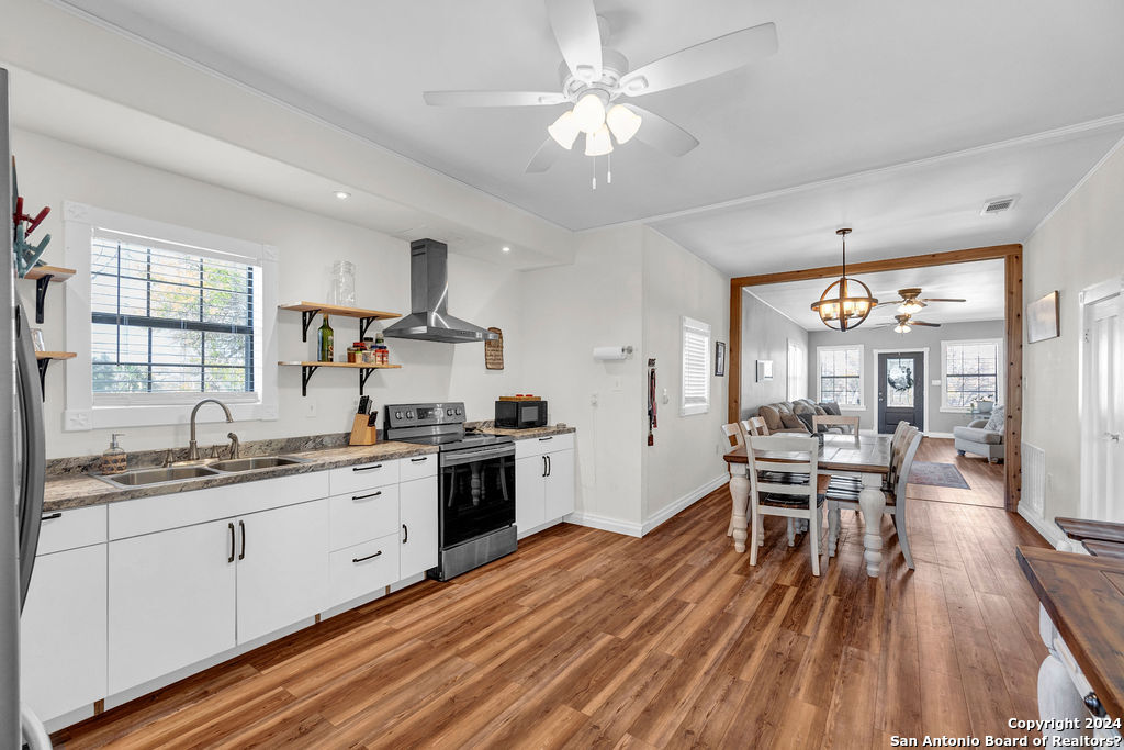 a open kitchen with stainless steel appliances granite countertop a stove top oven a sink dishwasher a dining table and chairs with wooden floor