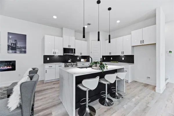 a kitchen with stainless steel appliances kitchen island granite countertop a sink a stove a refrigerator and white cabinets with wooden floor