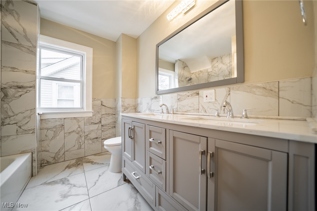 3816 Summit Park Road Cleveland Heights, OH 44121 - Photo 21 of 35 Bathroom featuring tile walls, wainscoting, light marble finish floors, double vanity, and a combined bath / shower with marble appearance