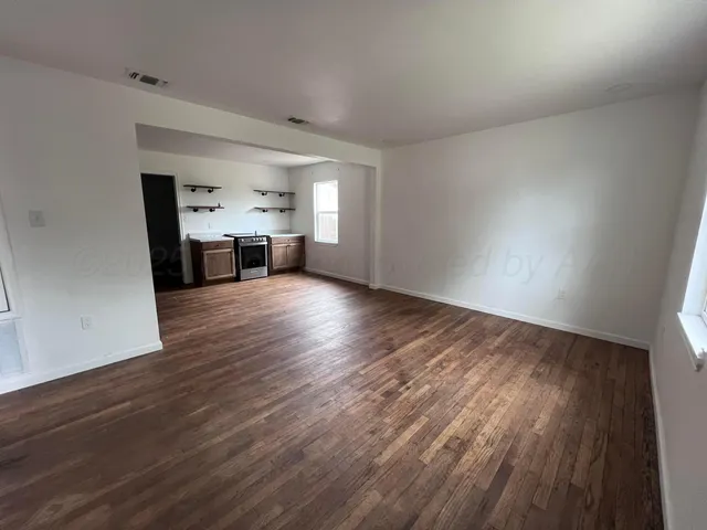an empty room with wooden floor kitchen view and a window