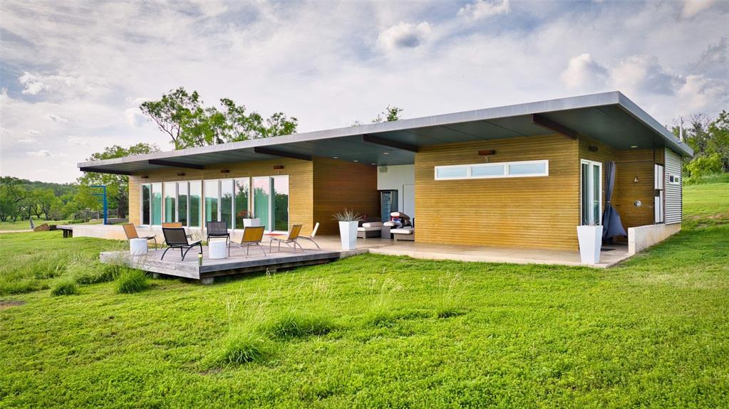 2969 County Lane Talpa, TX 76882 - Photo 6 of 40 Modern single-story residence featuring a flat roofline with deep overhangs, extensive wood-panel siding, a concrete foundation, and a spacious outdoor deck
