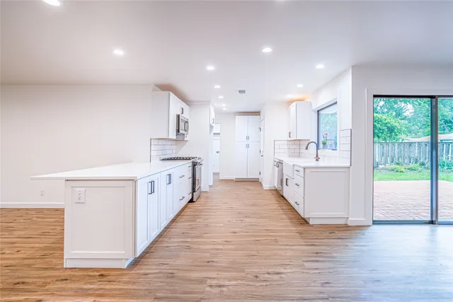 a large kitchen with a large counter top a sink stainless steel appliances and cabinets