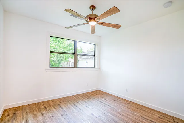 an empty room with wooden floor chandelier fan and windows