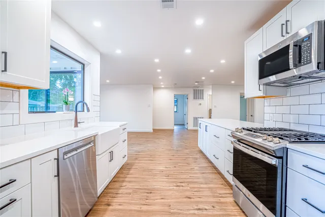 a large kitchen with stainless steel appliances kitchen island granite countertop a large stove a sink dishwasher and white cabinets with wooden floor