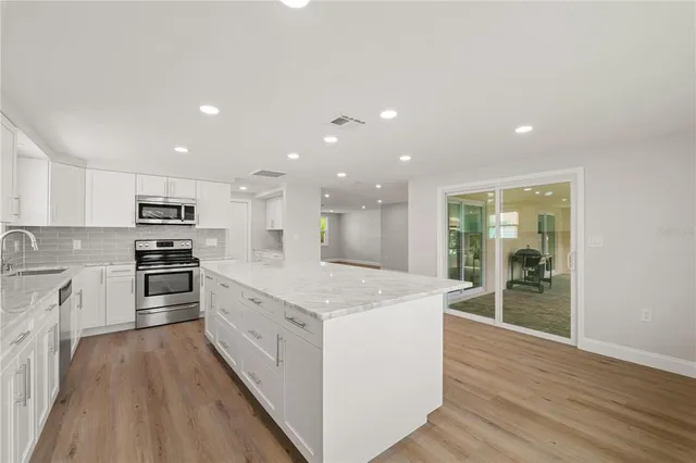 a large kitchen with kitchen island a stove a sink a refrigerator and white cabinets with wooden floor