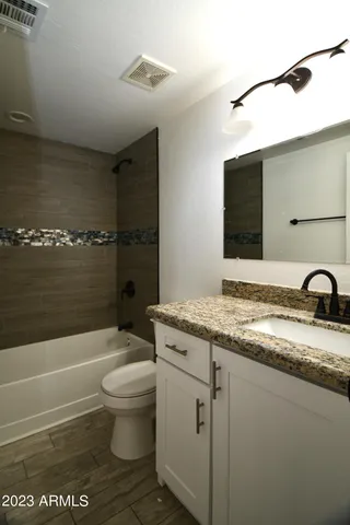 a bathroom with a granite countertop sink a toilet a mirror and bathtub