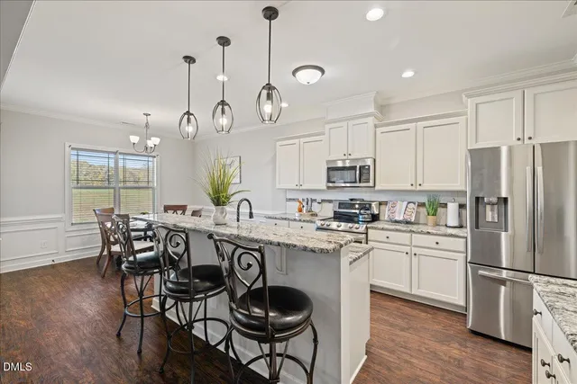 a kitchen with stainless steel appliances a dining table chairs a sink dishwasher a refrigerator cabinets and wooden floor