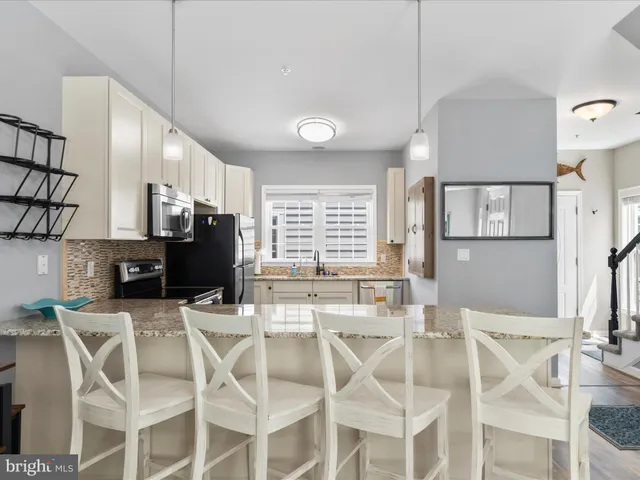 a dining room with stainless steel appliances kitchen island granite countertop a dining table chairs and a refrigerator