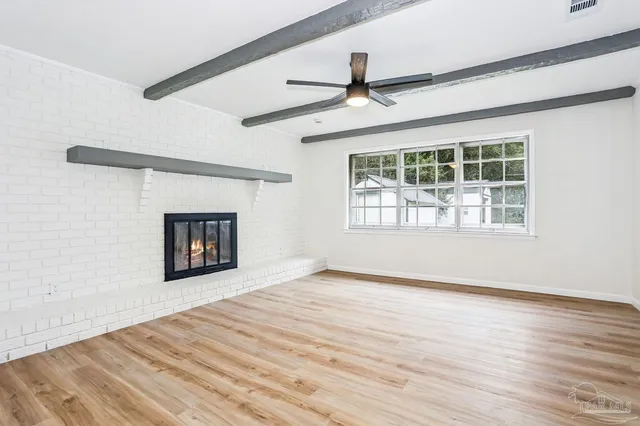 a view of an empty room with wooden floor fireplace and a window