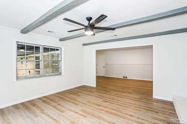 an empty room with wooden floor fan and windows