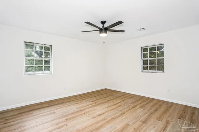 an empty room with wooden floor a ceiling fan and windows