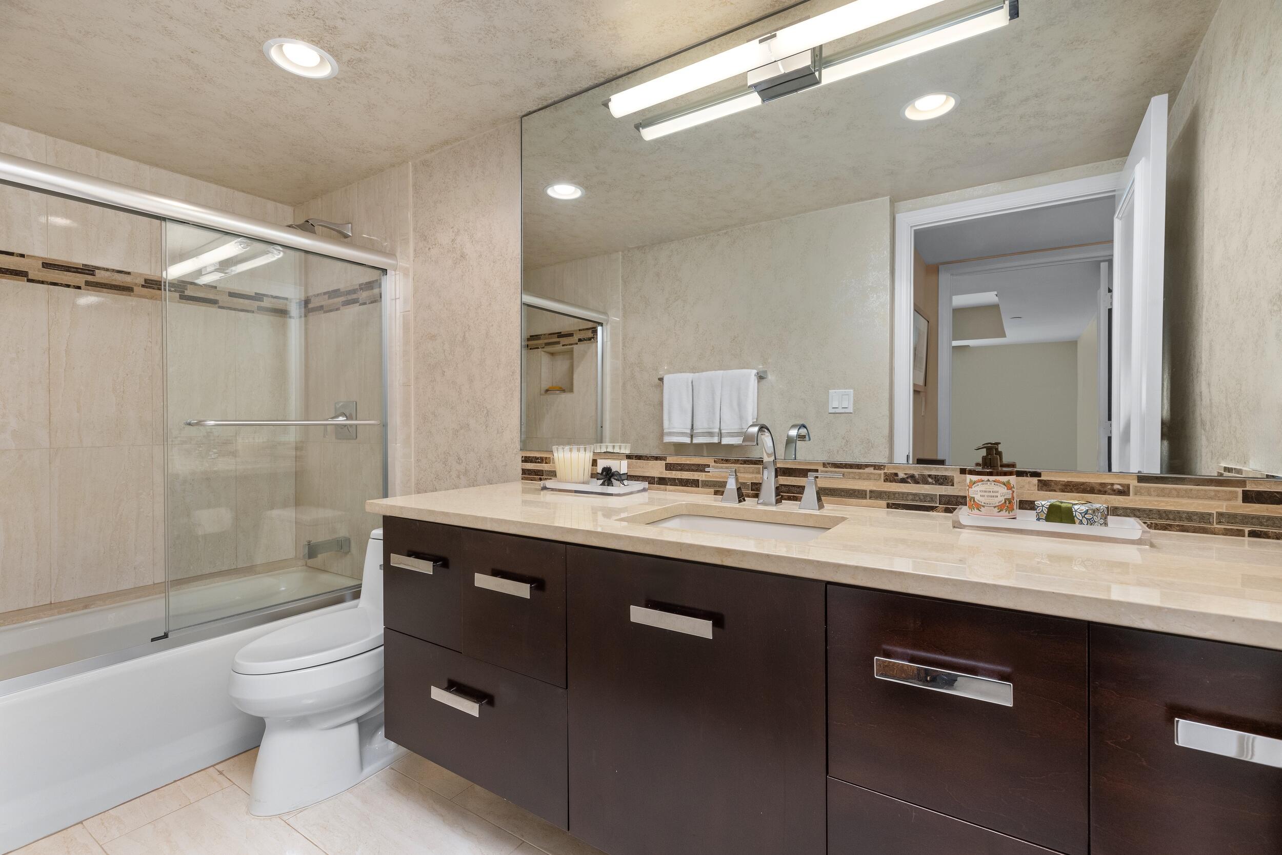 100 Southeast 5th Avenue, Unit 207 Boca Raton, FL 33432 - Photo 27 of 46 a bathroom with a granite countertop sink toilet a large mirror a bathtub and shower