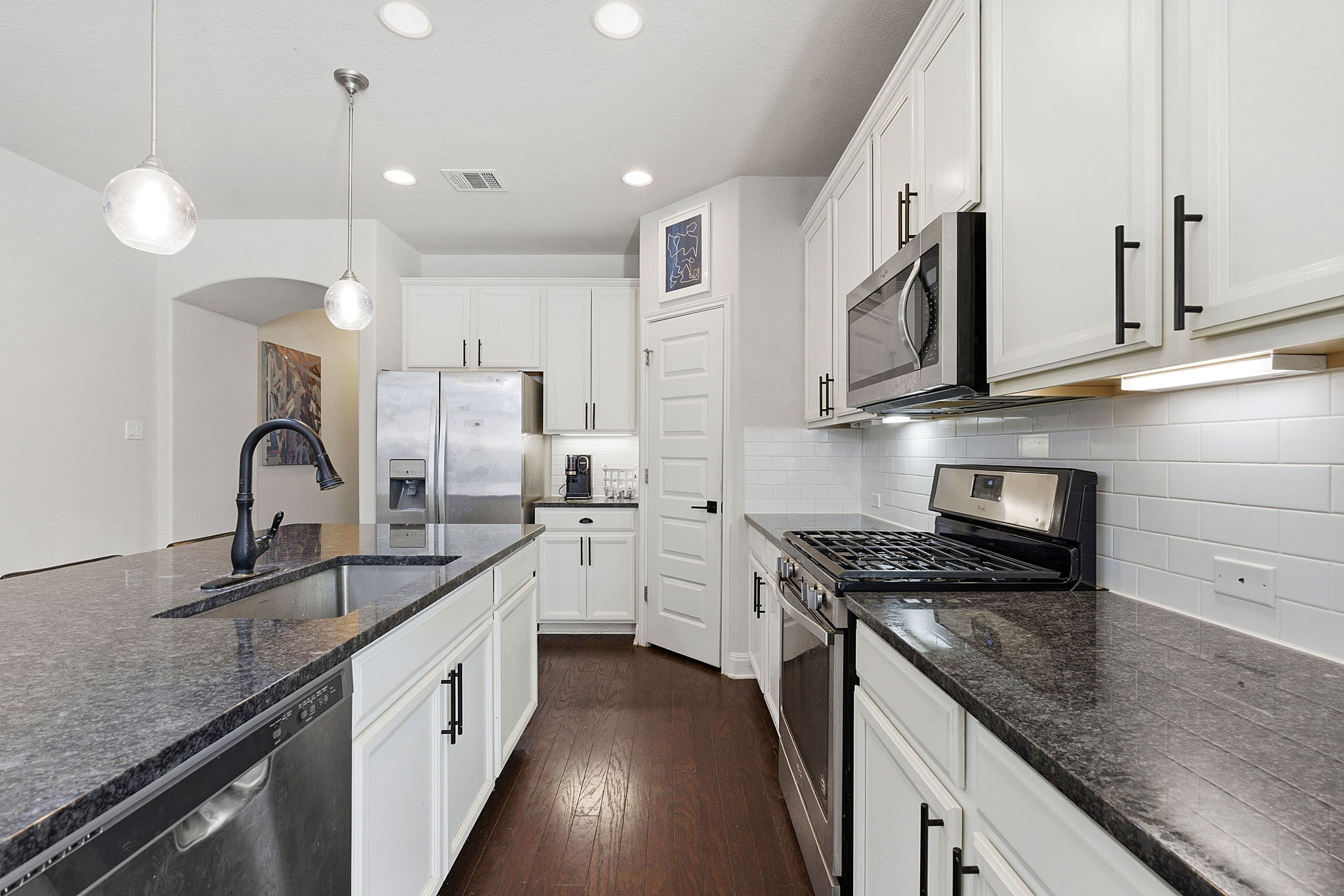 117 Methodius Drive Hutto, TX 78634 - Photo 9 of 40 Kitchen featuring stainless steel appliances, dark stone counters, dark wood-style flooring, hanging light fixtures, and white cabinetry