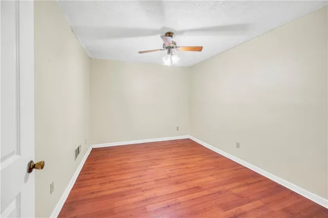 an empty room with wooden floor ceiling fan and window