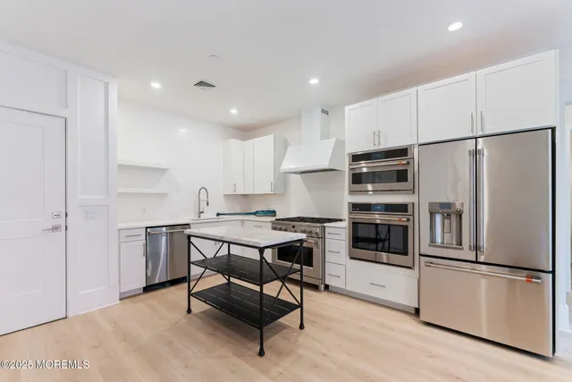 a kitchen with stainless steel appliances a refrigerator a stove a sink and white cabinets