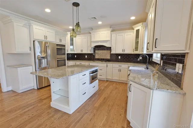 a large kitchen with stainless steel appliances granite countertop a stove top oven a refrigerator a sink and dishwasher with wooden floor